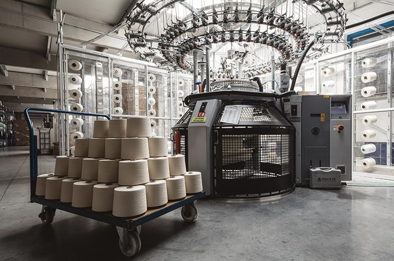 Circular knitting machine producing garment fabric on the factory floor